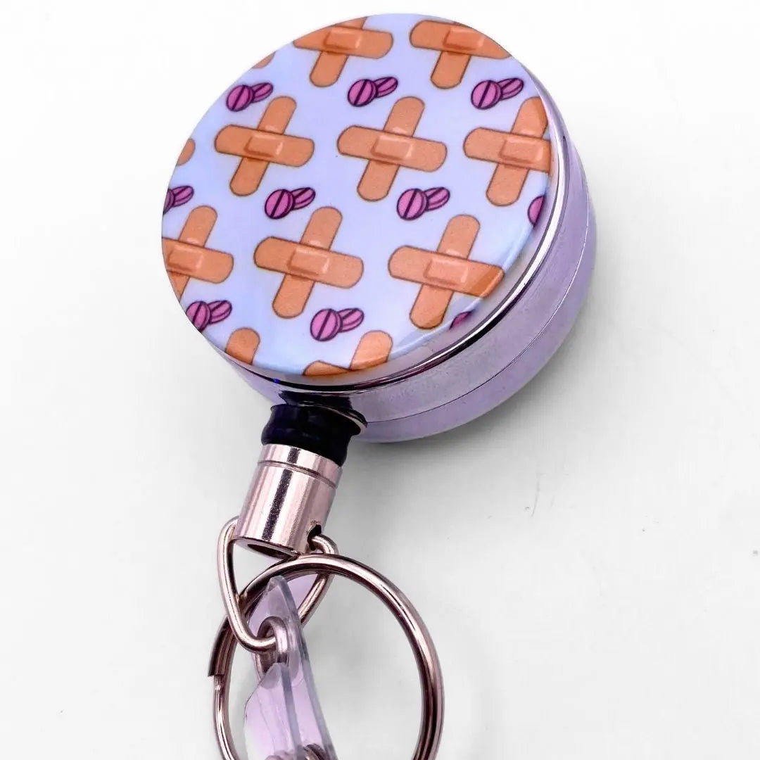 Nursing badge reel with a cartoon pattern of bandaids and medication on the front.