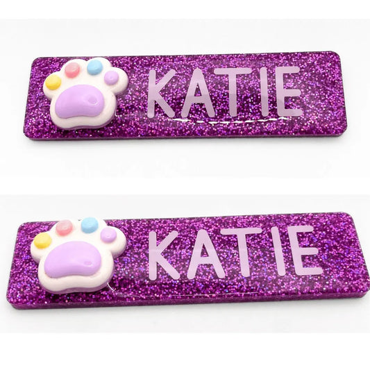 two purple glitter name tags with a cat paw